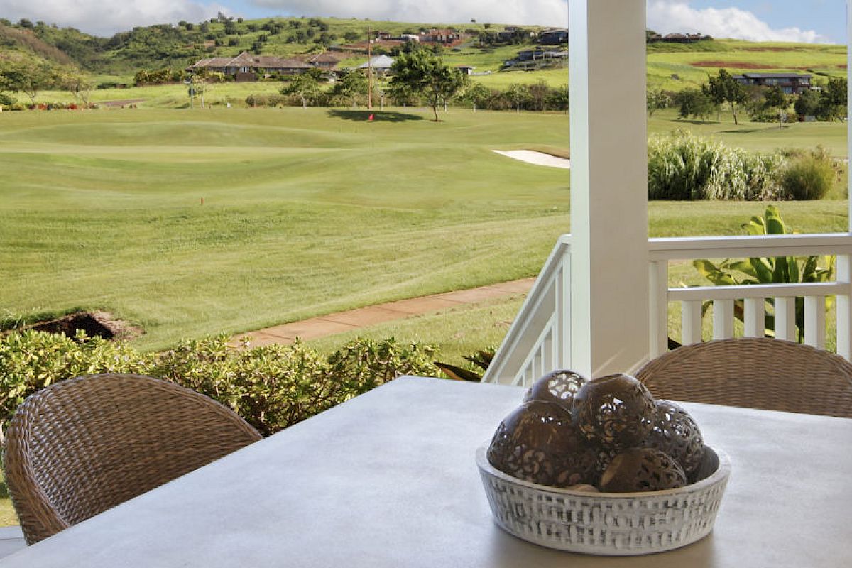 A patio with a table and chairs overlooks a lush golf course. A basket with decorative balls sits on the table to the left of the image.