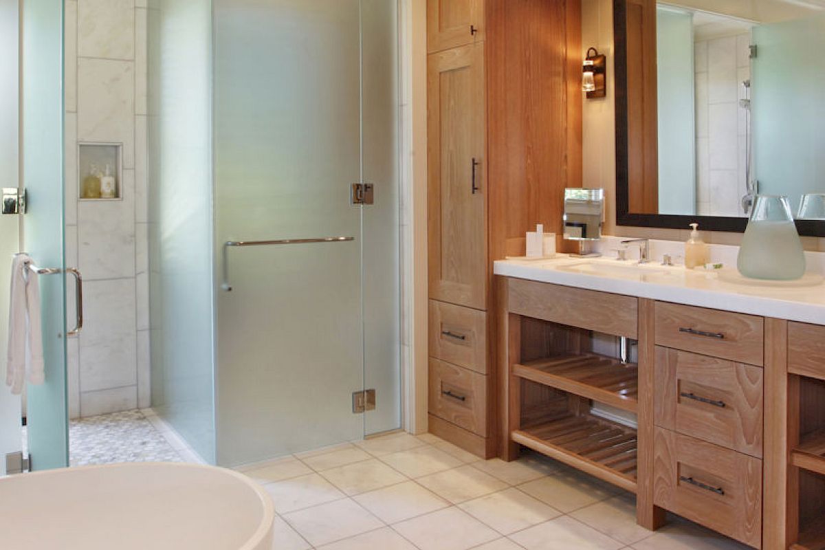 This image shows a spacious bathroom with frosted glass shower doors, a double vanity with wooden cabinetry, and a bathtub in the foreground.