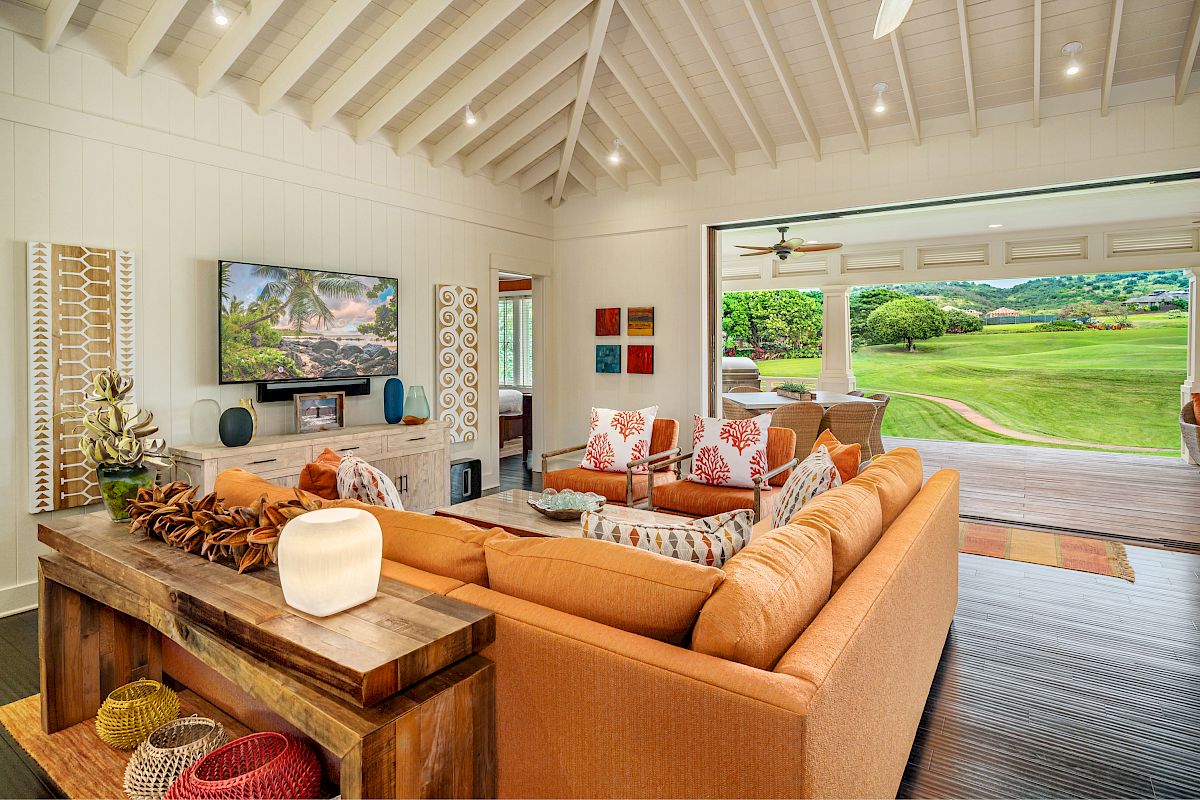 The image shows a stylish living room with bright decor, large windows, and a view of green landscapes outside. It's inviting and modern.