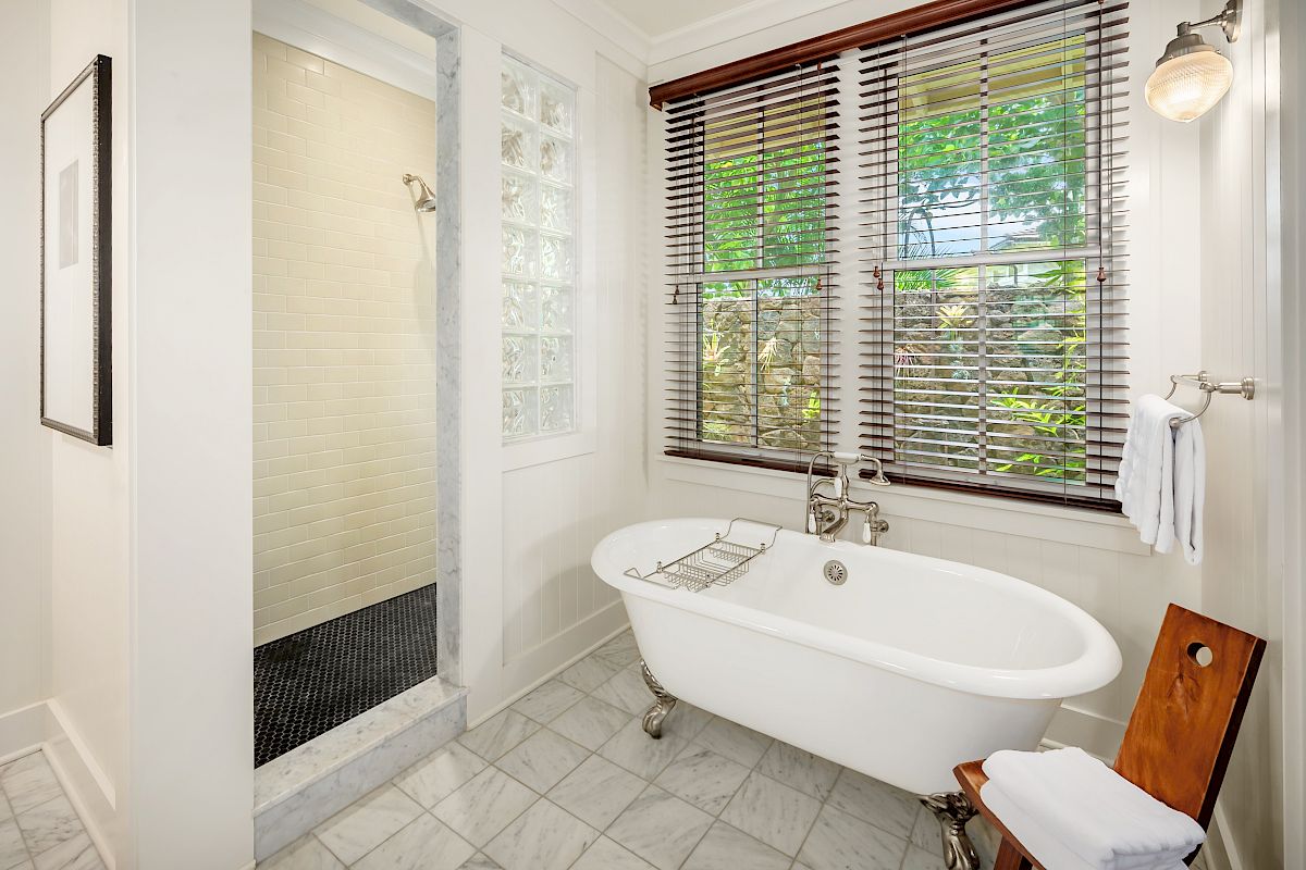 The image shows a modern bathroom featuring a freestanding bathtub, a shower area, and windows with a natural view.