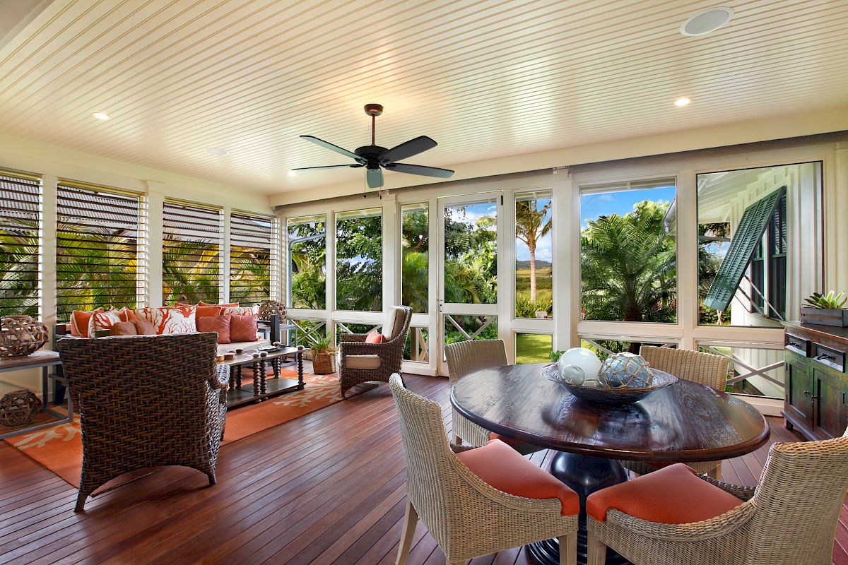 This image features a bright, airy indoor seating area with a round table, comfortable chairs, and large windows showcasing greenery.