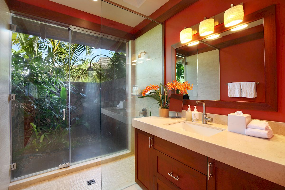 A modern bathroom with a glass-enclosed shower, a large mirror, a countertop with a sink, and a potted plant next to a window.