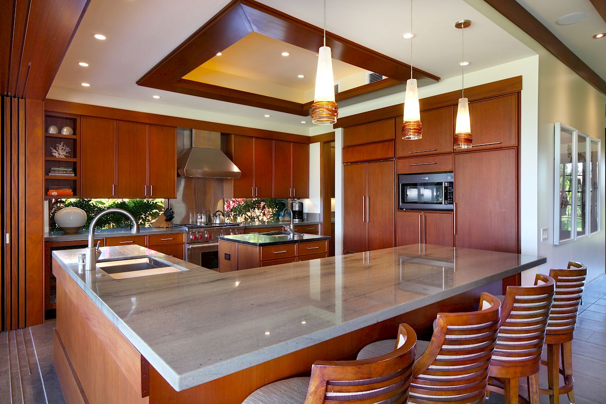 The image shows a modern kitchen with wooden cabinets, a large island, pendant lighting, and sleek appliances for a stylish look.