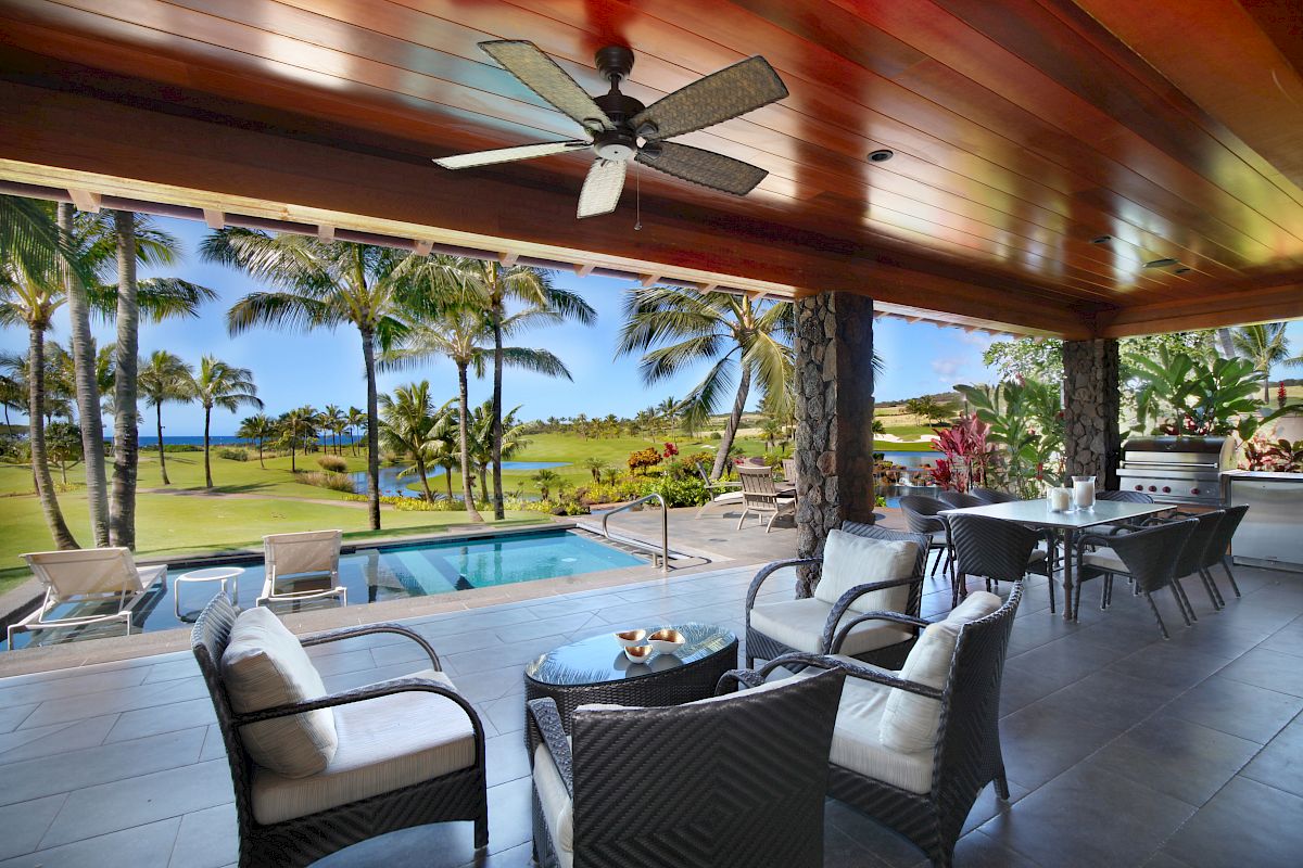 A luxurious patio with seating, a ceiling fan, a pool, and palm trees, offering a stunning view of the landscape outside.