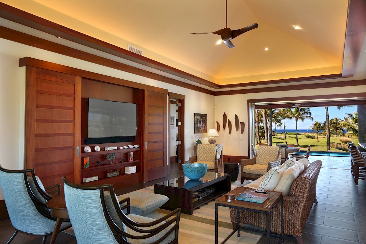 The image shows a stylish living room with modern furniture, large windows, and glimpses of a scenic outdoor view.