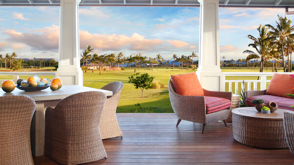 A spacious, elegantly furnished porch overlooking a lush golf course with palm trees under a cloudy sky, featuring wicker furniture and cozy seating.