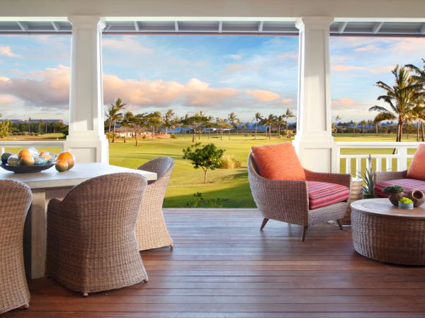 A spacious, elegantly furnished porch overlooking a lush golf course with palm trees under a cloudy sky, featuring wicker furniture and cozy seating.