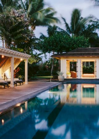 A luxurious poolside scene featuring lounge chairs, a gazebo, and lush tropical landscaping under warm, ambient lighting.