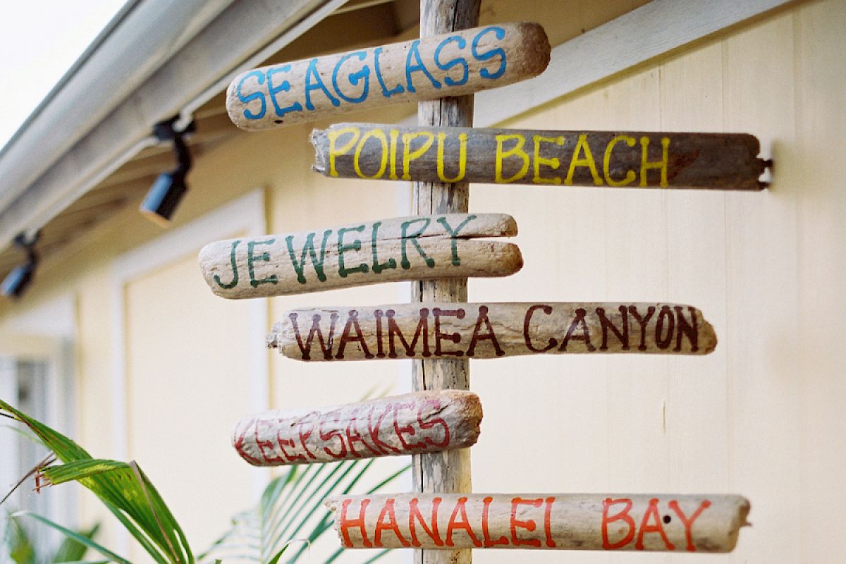 A wooden signpost with arrows pointing to Seaglass, Poipu Beach, Jewelry, Waimea Canyon, Kee Beach, and Hanalei Bay.