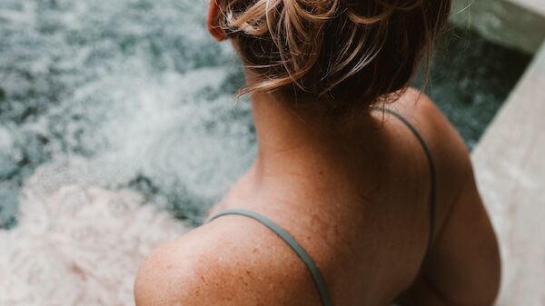 A person with their hair tied up is relaxing in a hot tub, facing away from the camera.