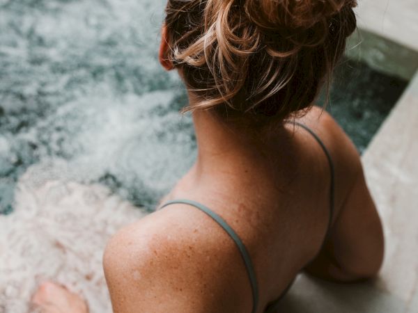 A person with their hair tied up is relaxing in a hot tub, facing away from the camera.