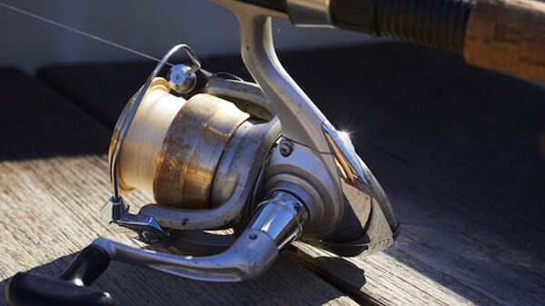 The image shows a fishing rod with a spinning reel resting on a wooden surface, likely outdoors.