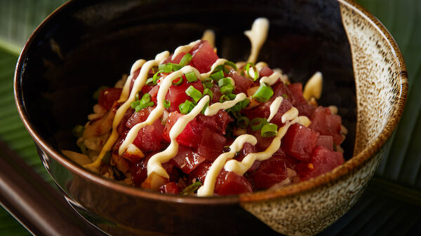 A bowl of diced raw fish topped with mayonnaise and chopped green onions, typically a dish known as poke, is displayed.