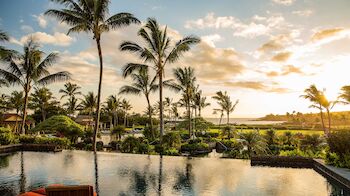 A serene tropical resort scene at sunset featuring palm trees, calm water, and loungers by a luxurious pool.