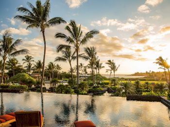 A serene tropical resort scene at sunset featuring palm trees, calm water, and loungers by a luxurious pool.