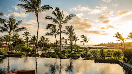 A serene tropical resort scene at sunset featuring palm trees, calm water, and loungers by a luxurious pool.