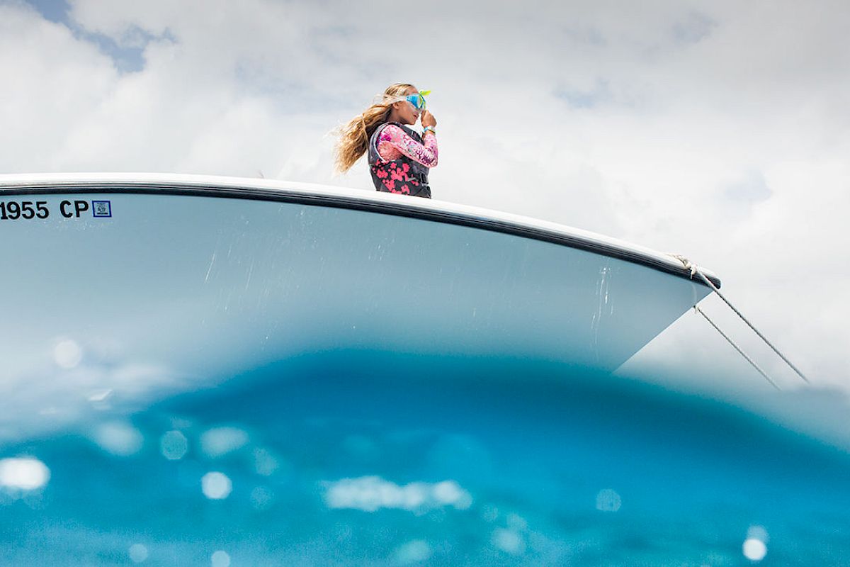 A person wearing a life jacket and mask is standing on a boat with the registration "HA 1955 CP" partially submerged in water.