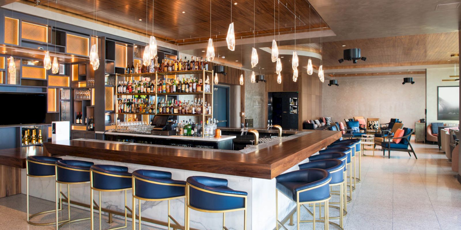 This image shows a modern bar with wooden and metallic decor, stylish seating, hanging lights, and a fully stocked bar counter. The ambiance is cozy.