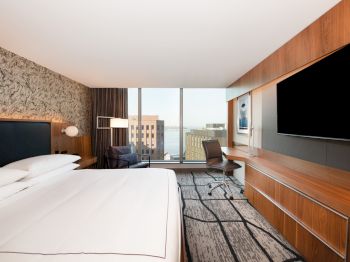 A modern hotel room featuring a large bed, a flat-screen TV, a desk with a chair, a seating area, and a window with a city view ending the sentence.