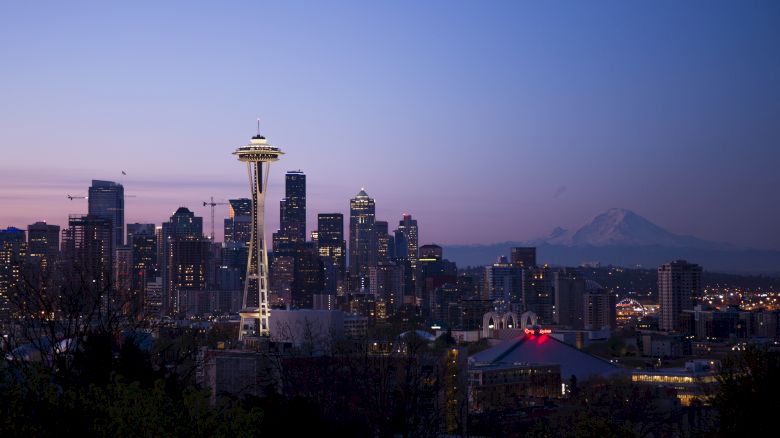 This image shows the skyline of Seattle at dusk, featuring the Space Needle prominently and Mount Rainier in the background against the fading light.